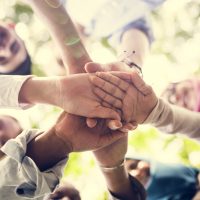 Image from below of young people joining hands in a circle.